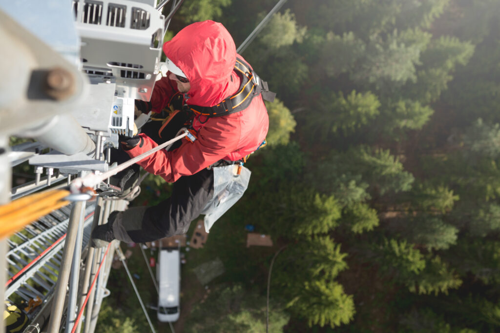 A man in red climbs a communications tower with trees below