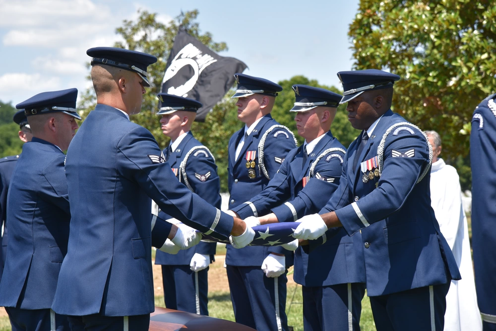 Air Force Service Members dressed in their Fine blue uniforms lower a triangle folded american flag over a casket
