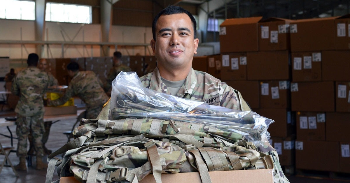 an army soldier holds a stack of camo clothing to give out to troops