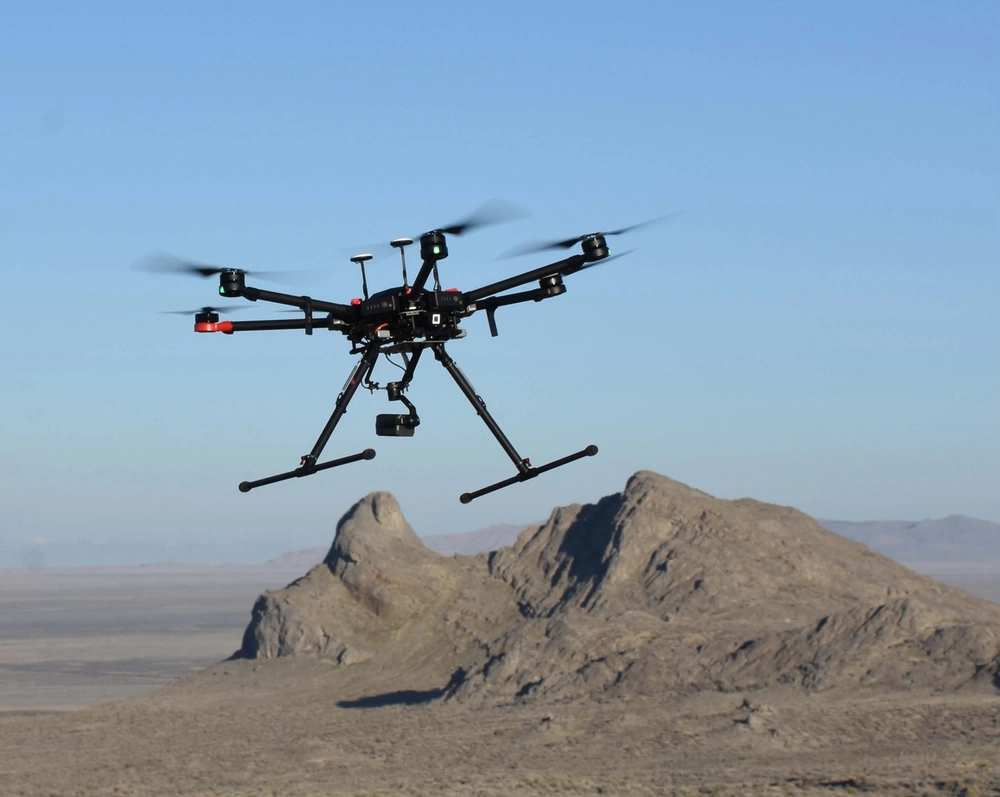 a military drone flies over some desert hills
